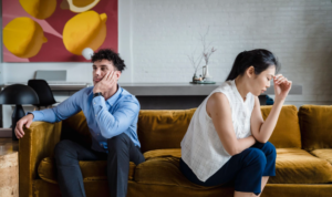 Exhausted couple sitting apart on a couch, considering marriage counseling in Mesa, AZ