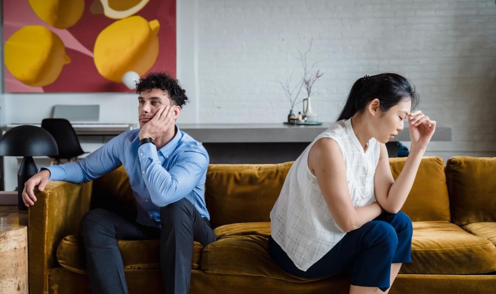 Exhausted couple sitting apart on a couch, considering marriage counseling in Mesa, AZ
